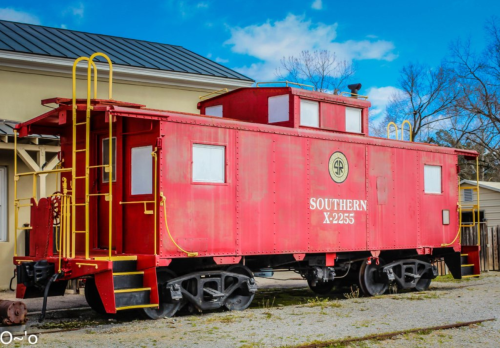 A bright red caboose labeled "Southern X-2255" displayed outdoors against a blue sky.