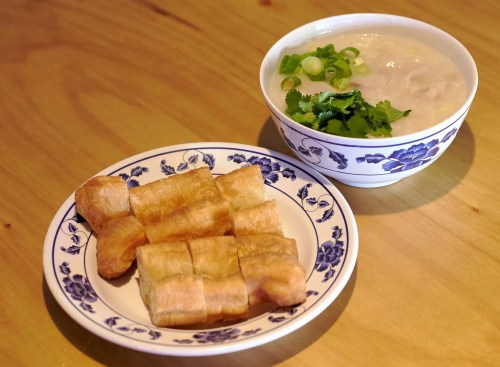 A plate of golden fried dough sticks next to a bowl of creamy porridge topped with green onions and cilantro.
