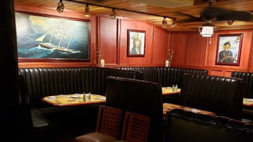 Cozy restaurant interior with dark booths, nautical paintings, and wooden accents.