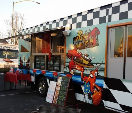 A colorful food truck with a checkered design, featuring a crab graphic and a menu board outside.