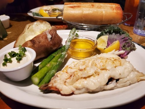 A plate featuring grilled fish, baked potato, asparagus, lemon, and a side of dipping sauce.