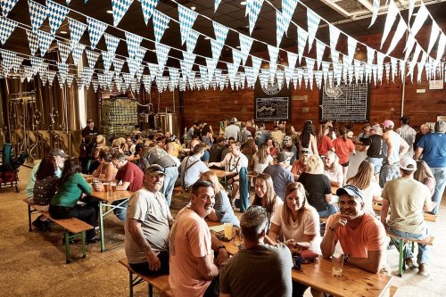 A lively brewery scene with a large crowd enjoying drinks, decorated with blue and white bunting.