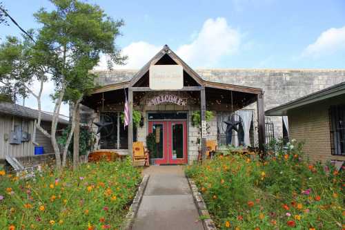 A charming building with a welcoming entrance, surrounded by colorful flowers and greenery under a blue sky.