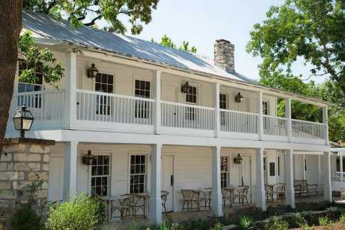 A charming white two-story building with a metal roof, featuring balconies and outdoor seating surrounded by greenery.