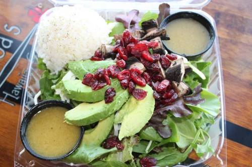 A fresh salad with avocado, cranberries, mushrooms, and rice, served with two small containers of dressing.