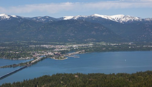 A scenic view of a lake surrounded by mountains, with a town and a bridge visible in the foreground.