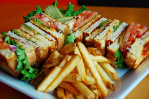 A plate of stacked sandwiches with lettuce, tomato, and fries on the side, garnished with pickles.