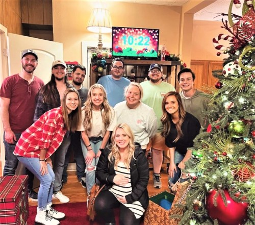 A group of ten people poses together in a festive room decorated for the holidays, with a Christmas tree and clock in the background.