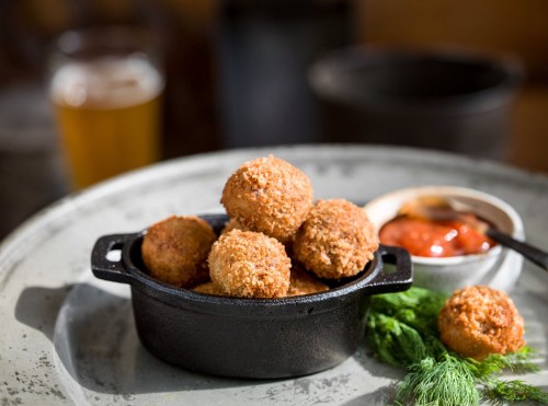 A cast iron dish filled with golden-brown fried balls, served with dipping sauce and garnished with fresh herbs.