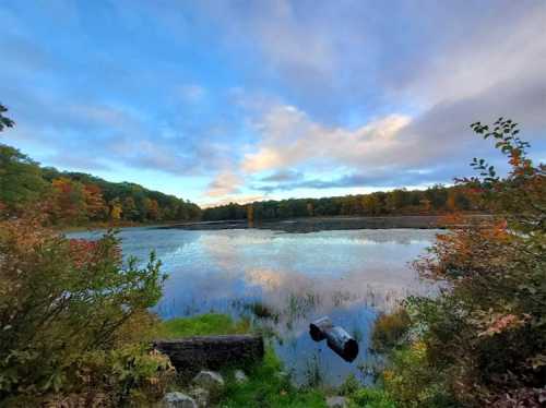 A serene lake surrounded by colorful autumn foliage under a partly cloudy sky.