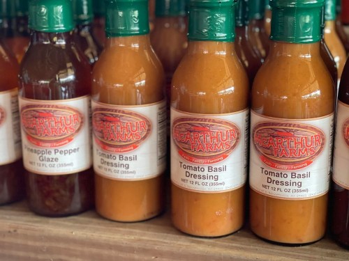 Bottles of various sauces and dressings lined up on a shelf, featuring labels for Pineapple Pepper Glaze and Tomato Basil Dressing.