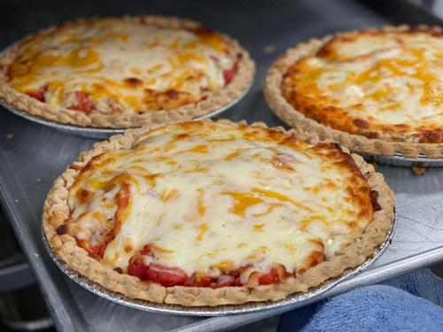 Three freshly baked pizzas with golden cheese and a crispy crust on a metal tray.