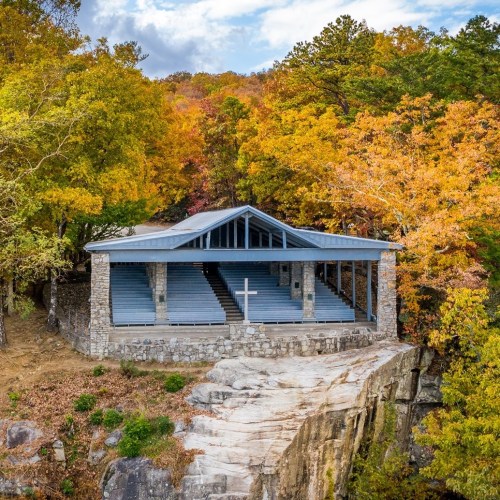 A stone pavilion with a cross overlooks a rocky cliff, surrounded by vibrant autumn foliage.