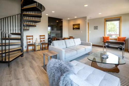 Modern living room with a spiral staircase, gray sofa, glass coffee table, and orange accent pillows. Bright and inviting space.