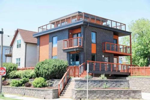Modern two-story house with a mix of dark brick and orange accents, featuring balconies and a landscaped yard.