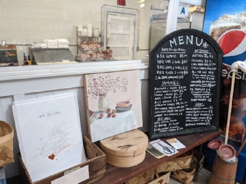 A menu board with food items and prices next to a decorative print and wooden containers in a casual dining setting.