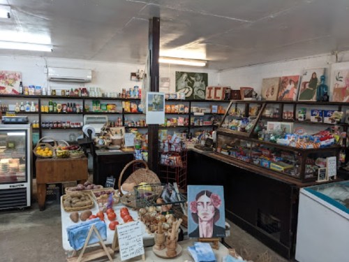 A cozy, vintage grocery store filled with shelves of food items, artwork, and a display of fresh produce.