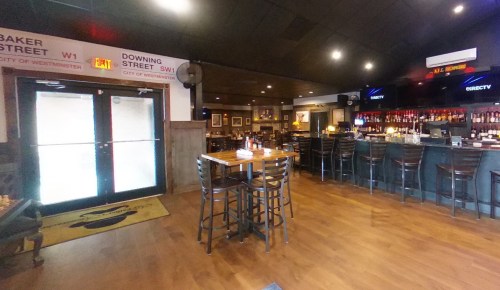 Interior of a restaurant featuring a bar, wooden tables, and a welcoming entrance with street signs on the walls.