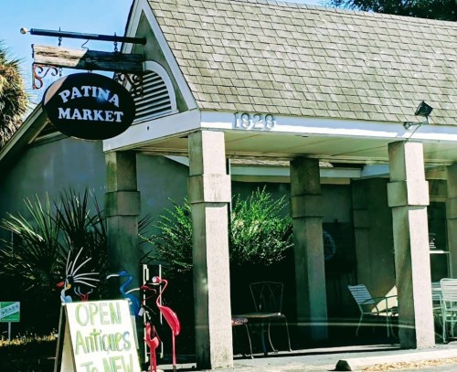 A storefront with a sign reading "Patina Market," featuring outdoor seating and a sign advertising antiques.