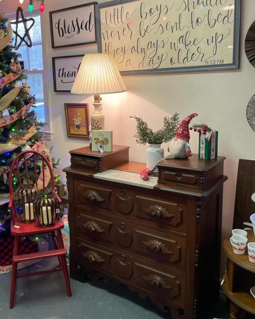A cozy holiday scene featuring a decorated Christmas tree, a lamp on a wooden dresser, and festive decor.