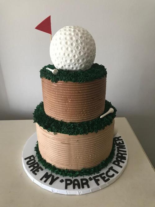A two-tiered cake designed like a golf course, featuring a golf ball, flag, and grass details. Text reads "Fore my 'par'fect partner."