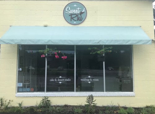 Exterior of "Sweet Rhu" cake and dessert studio, featuring a green awning and window displays with flowers.
