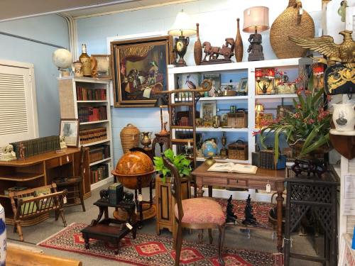 A cozy antique shop filled with vintage furniture, books, globes, and decorative items on shelves and tables.