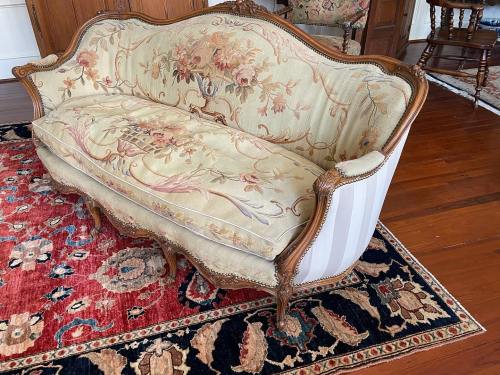 A vintage floral-patterned sofa with ornate wooden details, placed on a decorative rug in a cozy room.