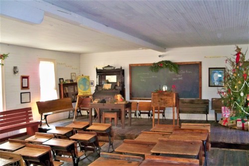 A vintage classroom with wooden desks, a chalkboard, and a decorated Christmas tree in the corner.