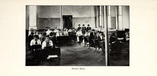 Black and white image of a study hall with students seated at desks, focused on their work.