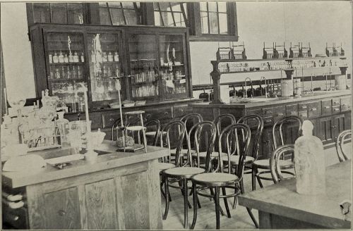 A vintage laboratory with wooden furniture, glassware, and shelves filled with bottles and scientific equipment.