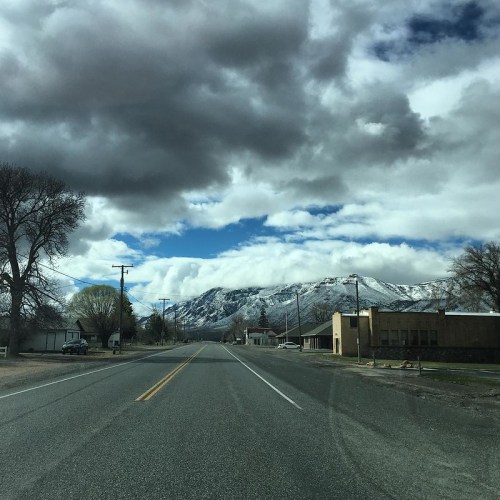 A scenic view of a road leading towards snow-capped mountains under a partly cloudy sky.
