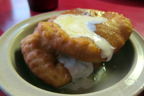 Two golden fried pastries stacked on a plate, drizzled with a creamy sauce.