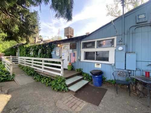 A blue building with a wooden walkway, surrounded by greenery, featuring an American flag and outdoor seating.