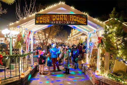 A festive night scene at John Dunn House Shops, bustling with people and colorful holiday lights.
