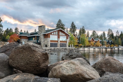 A scenic lakeside view featuring modern homes surrounded by trees and rocky shoreline under a cloudy sky.