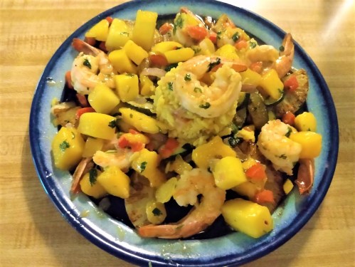 A colorful dish featuring shrimp, diced mango, and vegetables, served on a blue plate.