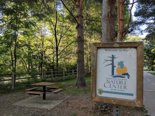 Sign for Morrison Knudsen Nature Center with a picnic table and trees in the background.