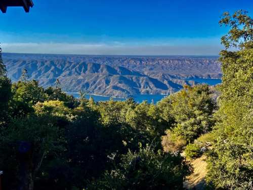A scenic view of rolling hills and a lake, framed by lush greenery under a clear blue sky.