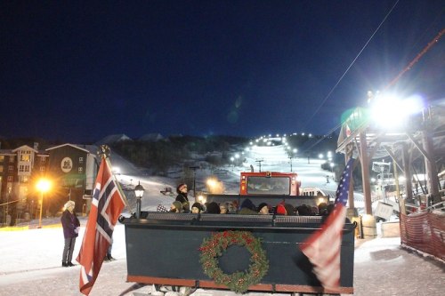 A festive sleigh with flags parked at a snowy ski resort, illuminated by lights against a night sky.