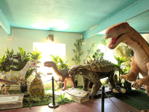 A colorful display of dinosaur models surrounded by plants, set in a brightly lit room.