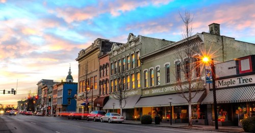 Historic buildings line a street at sunset, with colorful skies and streetlights illuminating the scene.