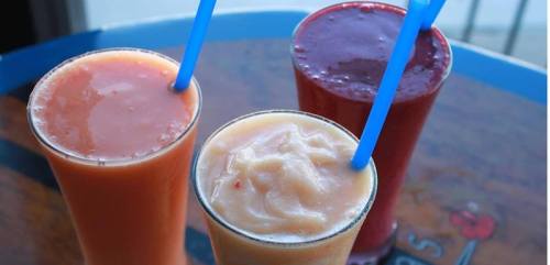 Three colorful smoothies in glasses with blue straws, featuring orange, cream, and berry flavors.