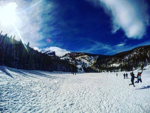 A snowy landscape with people enjoying the outdoors, surrounded by mountains and a bright blue sky.