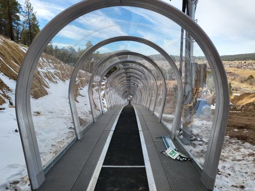 A clear, curved tunnel structure with a metal frame, set in a snowy landscape, leading into the distance.