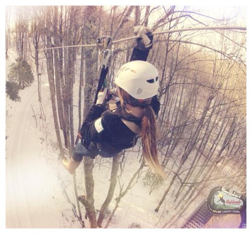 A person zip-lining through a snowy forest, wearing a helmet and harness, with trees in the background.