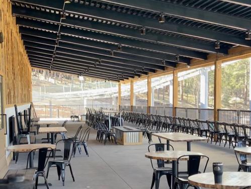 A spacious outdoor seating area with metal tables and chairs under a covered patio, surrounded by trees.