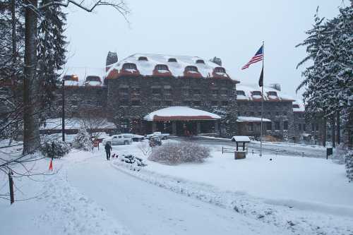 A snow-covered hotel with a stone facade, surrounded by trees, and an American flag flying in the winter landscape.