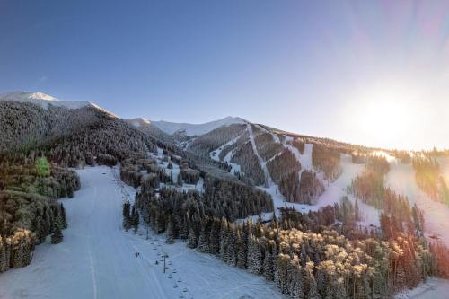 A scenic winter landscape featuring snow-covered mountains, ski slopes, and a bright sun rising in the background.