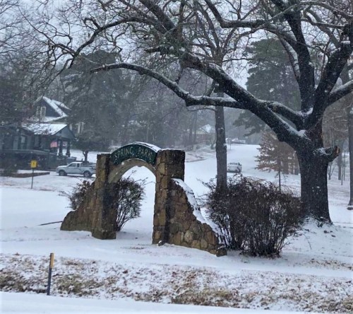 Snow-covered entrance to Spring Park, framed by trees and a quiet, wintery street.